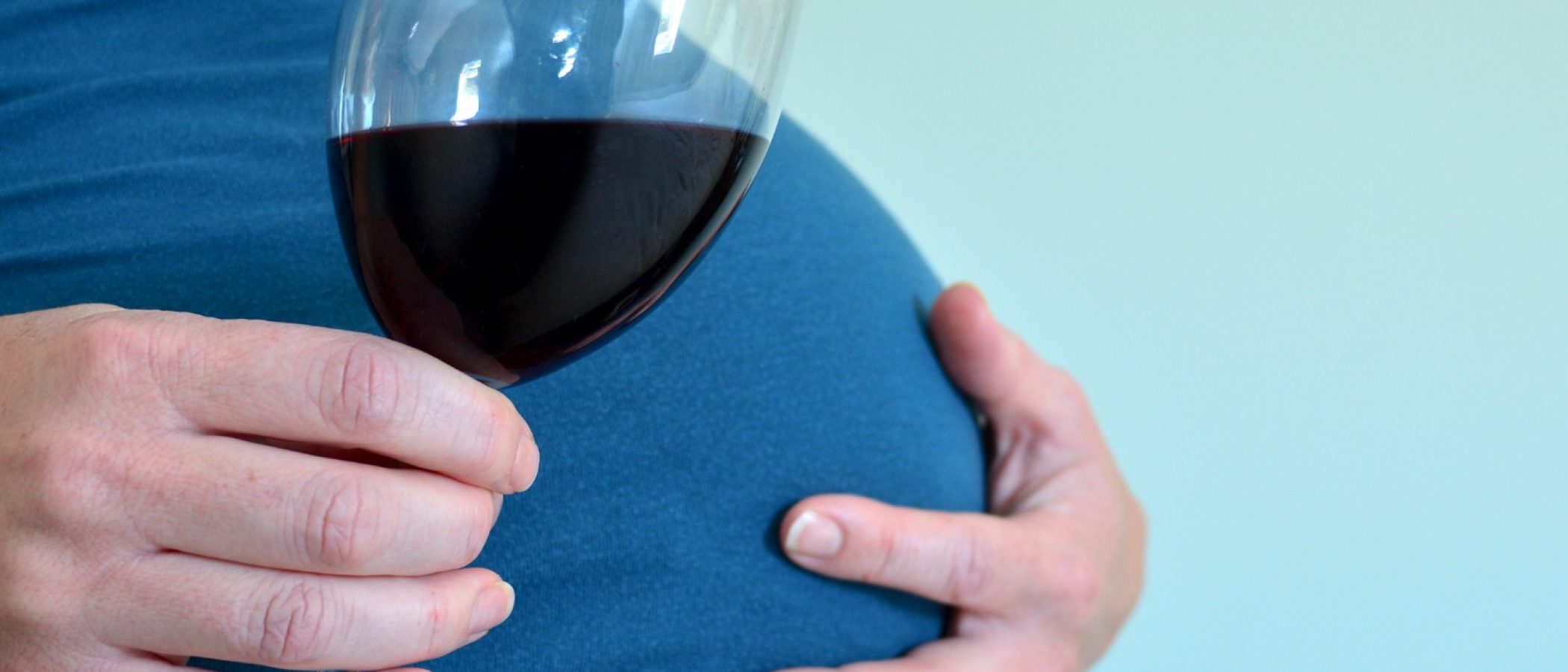close up of pregnant woman’s belly, while she is holding a glass of red wine - fetal alcohol syndrome